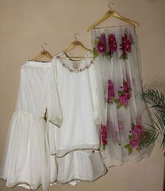 three white dresses hanging on a rack with pink flowers