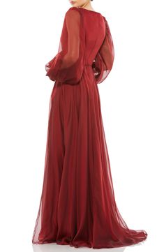 a woman in a long red dress with sheer sleeves and an open back, standing on a