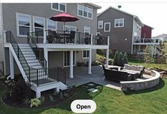 an outdoor patio with seating and umbrella in front of two story house on grassy area