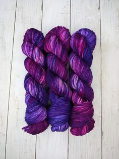 three skeins of purple yarn sitting on top of a white wooden floor next to each other