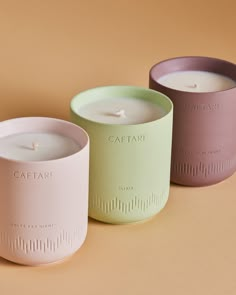 three candles sitting next to each other on top of a brown surface with the words catafari written in white