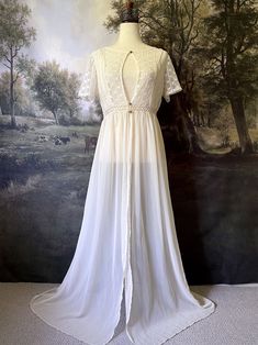 A historically inspired Edwardian era Ivory maxi Overdress with Floral Lace Details is pictured on a mannequin in front of an art history backdrop. Bohemian Chiffon Dress With Lace Trim, Cream Floor-length Gown With Lace Trim, White Spring Gown With Sheer Bodice, Spring White Gown With Sheer Bodice, Chiffon Dress With Lace Trim For Garden Party, Chiffon Lace Trim Dress For Garden Party, Spring Dresses With Lace Patchwork And Flowy Skirt, White Sheer Bodice Gown For Spring, Long Lace Gown With Lace Trim