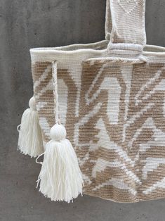 a white and beige bag with tassels hanging from it's side on a concrete wall