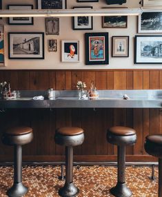 the bar has four stools in front of it and many framed pictures on the wall