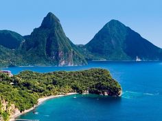 an island surrounded by mountains in the middle of the ocean with boats floating on it