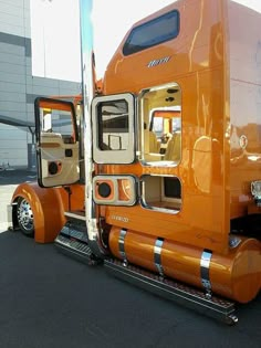 an orange semi truck parked in front of a building with its doors open and the door ajar