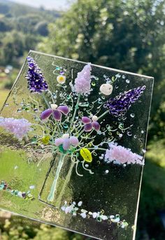 a glass vase with flowers in it sitting on top of a window sill next to trees