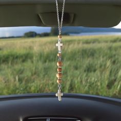 a car dashboard with a cross hanging from it's dash board in front of a grassy field