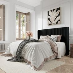 a bedroom with white walls and wooden floors, a bed in the center has a black headboard