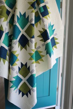 a quilted blanket hanging on a blue door with white and green colors in the background