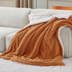 a white couch with an orange blanket on top of it next to a brown and white pillow