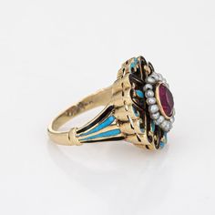 This is part of Chairish’s Fine Jewelry assortment.  Elegant and finely detailed Edwardian era enamel ring (circa 1900s to 1910s), crafted in 14 karat yellow gold.    Created ruby measures 5mm (in very good condition and free of cracks or crisps). Small natural 1mm seed pearls surround the ruby.   A created ruby is set into a beautifully detailed scrolled mount. Blue and black enamel adds a pop of colour, offering contrast to the ruby that is striking and unique. The ring is small in size (2 1/2 Vintage Gold Enamel Ring Stamped 14k, Victorian Enamel Ring For Anniversary, Victorian Style Hallmarked Enamel Ring For Anniversary, Victorian Gold Enamel Ceremonial Ring, Victorian Yellow Gold Enamel Ring, Victorian Oval Enamel Ring For Anniversary, Victorian Yellow Gold Enamel Ring For Anniversary, Antique 14k Gold Ruby Ring With Intricate Design, Antique Enamel Ring With Rose Cut Diamonds