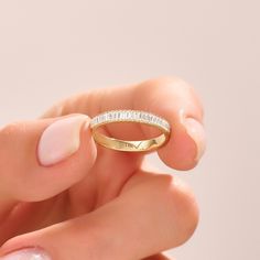 a woman's hand holding a yellow gold ring with white diamonds on the side