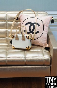 a small purse sitting on top of a couch next to a pillow with a chanel logo on it