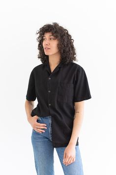 "Vintage black short sleeve shirt with great simple collar, 4 snap buttons, one front rounded patch pocket. Simple addition to any wardrobe and a great transitional piece. Maker: Military Made in the USA in the 60s. Garment Dyed in Los Angeles in 2019. Material: 100% Cotton. Condition: Two Options : Good with some small repairs that include darning. OR Small Holes and scuffs. Not perfect. Measurements: X- SMALL: Shoulder: 16\" | Chest: 17-18\" | Length: 27\" | Sleeve: 9.5\" SMALL: Shoulder: 17\" Relaxed Fit Solid Camp Shirt With Buttons, Relaxed Fit Camp Shirt With Buttons, Relaxed Fit Shirt With Buttons For Everyday, Relaxed Fit Shirt For Everyday, Casual Black Button-up Short Sleeve Shirt, Unstructured Black Tops With Pockets, Black Cotton Short Sleeve Shirt With Buttons, Black Relaxed Fit Tops With Buttons, Black Cotton Short Sleeve Casual Shirt