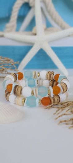 two bracelets with beads and seashells on a white table next to a starfish