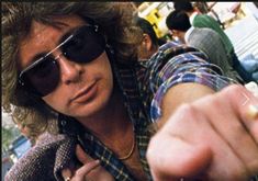 a man in sunglasses pointing at something with his finger on the other side of him