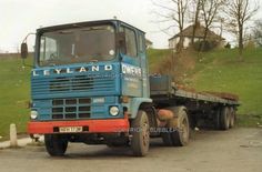 a blue and red truck parked on the side of a road next to a lush green hillside