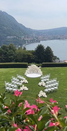 an outdoor ceremony set up with white chairs and pink flowers on the grass near water