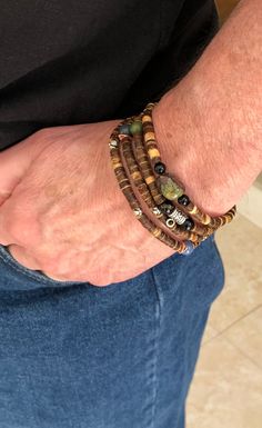 This wood-beaded item serves as both a necklace and a bracelet and can be worn three ways. The necklace is 36 1/2 inches long and can wrap around a man's wrist 3 or 4 times depending on the person's hand and wrist size. It will wrap around a 7 1/2 inch wrist 4 times. It is beaded on a stretch cord that fits over the head, and the  necklace has two ends. 4mm wood beads form most of the cord. A genuine bloodstone gem sits in the center of two black obsidians and forms one end of the necklace. Blue aventurine, green jade and silver and copper spacer beads serve as accents between the wooden beads. At the closure is a silver barrel shaped bail. Here you can wear a charm or pendant of your choosing. Though pictured, a pendant does not come with the necklace. I have enclosed two jump rings to at Festival Brown Gemstone Beaded Bracelets, Festival Brown Beaded Bracelets With Gemstone, Brown Gemstone Beaded Bracelets For Festival, Hippie Style Brown Hand-strung Beaded Bracelets, Hippie Brown Jewelry With Natural Stones, Bohemian Hand Wrapped Beaded Bracelets, Casual Brown Hand Wrapped Jewelry, Bohemian Wrap Bracelet For Layering, Casual Hand Wrapped Brown Jewelry