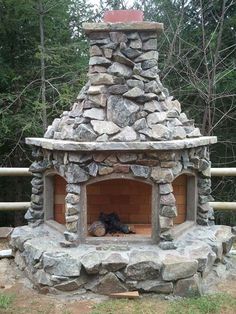 an outdoor fireplace made out of rocks in the woods