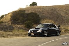 the black car is parked on the side of the road in front of a hill