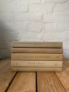 four books stacked on top of each other in front of a white brick wall and wooden floor