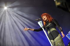 a woman standing in front of a microphone with her hands out and lights on behind her