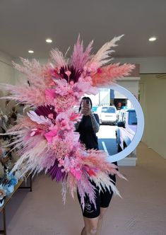 a woman standing in front of a mirror holding a pink and purple feathered arrangement