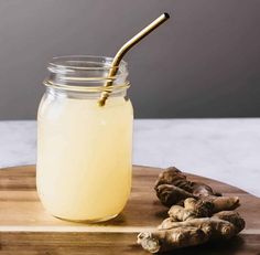 a glass jar filled with liquid next to some ginger root on a wooden cutting board