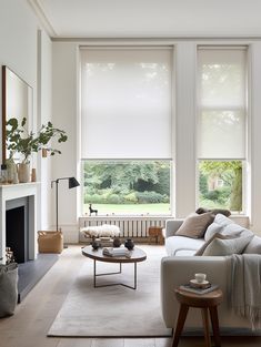 a living room with two large windows and a white couch in front of a fireplace