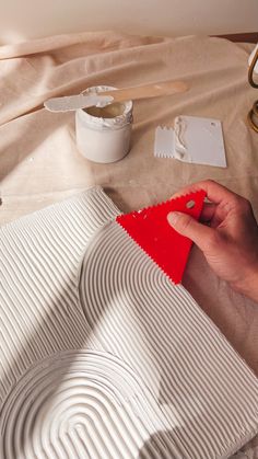 a person is painting a piece of paper on a table with other items around it