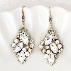 Escape into the understated elegance of yesteryears with our Marquise Crystal Wedding Earrings. Crafted for the bride with a passion for vintage charm, these earrings harmoniously blend the traditional with a modern flair. Inspired by the intricate leaves of an antique gold necklace, we have interlaced golden hues and bronzed tones to recreate that coveted heirloom look. The centerpiece features navette crystals nestled among delicate rhinestones, orchestrated to mimic the affected leaves of a t Elegant Vintage Charm Jewelry, Elegant Formal Earrings With Vintage Charm, Classic Dangle Jewelry For Vintage Events, Elegant Vintage Charm Earrings For Wedding, Elegant Vintage Charm Wedding Earrings, Classic Drop Earrings For Vintage Events, Elegant Vintage Charm Earrings For Formal Occasions, Elegant Vintage Charm Jewelry For Anniversary, Elegant White Jewelry For Wedding Reception