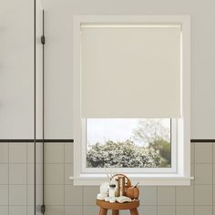 a bathroom window with roller shades on the top and bottom, next to a wooden stool in front of it