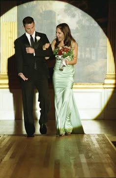 a man and woman in formal wear walking down a hall together, with the light shining on them