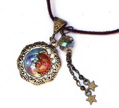 "A necklace with whimsical celestial charm featuring an embossed gold moon and sun pendant that's been accented with violet and pinked orange! Dangling alongside,a couple of star charms swing beneath a lustrous faceted glass bead of light turquoise! And a violet/moonstone-colored Swarovski crystal rhinestone sparkles from the half moons' chin! The artful pendant hangs from a faux suede necklace that has an extender chain to make it easy to find your perfect length! Add this one to your jewelry b Whimsical Star Charm Jewelry As Gift, Whimsical Star Charm Jewelry Gift, Whimsical Adjustable Round Pendant Necklace, Whimsical Round Pendant Necklace, Celestial Charm Necklace With Round Pendant, Vintage Sun And Moon Round Pendant Jewelry, Celestial Charm Necklace With Adjustable Round Pendant, Adjustable Star Charm Festival Jewelry, Vintage Sun And Moon Design Round Pendant Jewelry