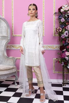 White and gold are preferred choices of Mughal princess. You can never go wrong with a classy white silhouette. Sylvia by Maria Nasir is a classic wardrobe piece for a reason! This elegant piece defines femininity and can make you look beautiful effortlessly. Sylvia is beautiful combination of pearl white and gold A-line shirt in paper cotton fabric. The boat neckline is dazzled with gold lace while the ¾ sleeves are also adorned with gold lace. Featuring the soft organza tulle dupatta in shades of pearl white and gold. The shirt is paired with a matching silk slip and beige pants with lace detailing. Accessorize this number with ethnic earring and bindya set for a flawless look. Top: Color: White Fabric: Paper cotton A shaped shirt with zari work all over Boat shaped neckline    Gold lace White Tissue Silk Kurta With Sheer Dupatta, Elegant Churidar With Sheer Dupatta For Navratri, Celebration Kurta With Sheer Dupatta In Raw Silk, Long Sleeve Tissue Silk Dress For Eid, Celebration Kurta With Dupatta In Tissue Silk, Tissue Silk Kurta With Dupatta For Celebration, Gold Long Sleeve Dresses For Diwali, Elegant Lawn Suit With Dabka For Wedding, Gold Long Sleeve Semi-stitched Dress