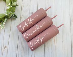 three pink personalized travel mugs with writing on them sitting next to some flowers