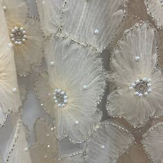 some white flowers and pearls are on a sheer lace fabric with beadings in the center