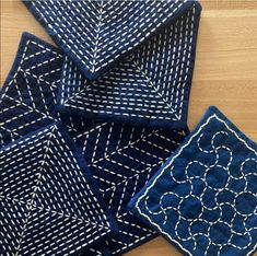 four blue napkins with white stitching on them sitting on a table next to each other