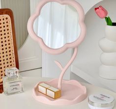 a pink mirror sitting on top of a table next to a vase with a flower