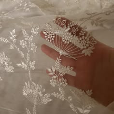 a person's hand holding some white lace on a bed sheet with flowers and leaves