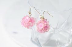 small pink flowers are hanging from earrings on a clear glass stand in front of a white background