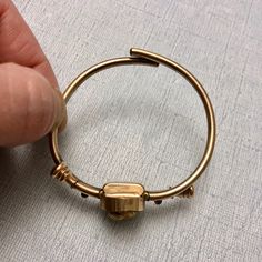 a person is holding a gold ring with a square shaped object on it's side