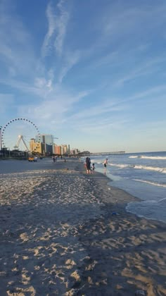 people are walking on the beach with ferris wheel in the background