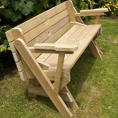 a wooden bench sitting on top of a green grass covered park field next to bushes