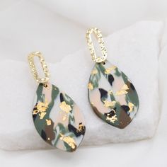 a pair of earrings with gold leaf designs on them sitting on a white cloth covered surface