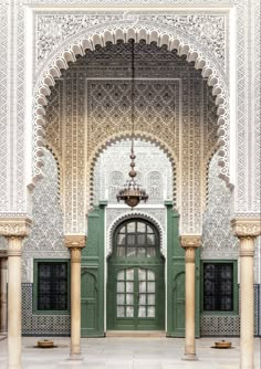 the entrance to an ornate building with green doors and pillars, in front of a chandelier