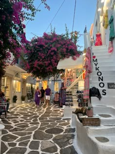 people are walking down the street in front of shops with flowers growing on the walls