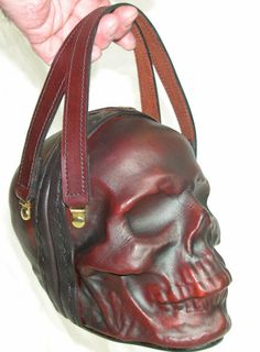 a handbag with a skull head on the front and side, held by a woman's hand